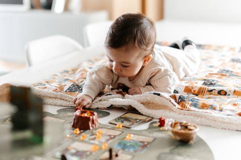 Close da bebê de bruços na mesa olhando curiosa para os pais jogando. '