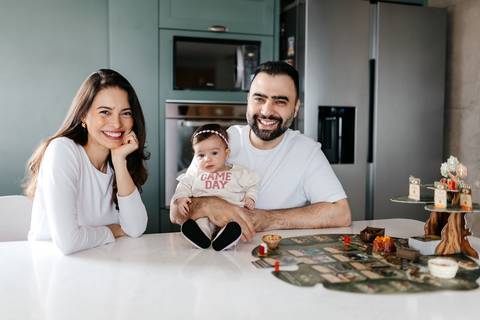 Retrato oficial dos pais e da bebê sentados juntos na mesa da cozinha.'