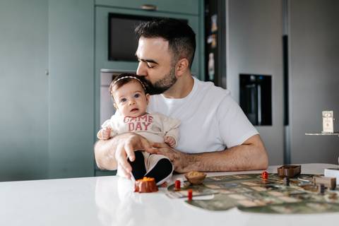 Pai dando um beijo carinhoso na cabeça da bebê no colo.'