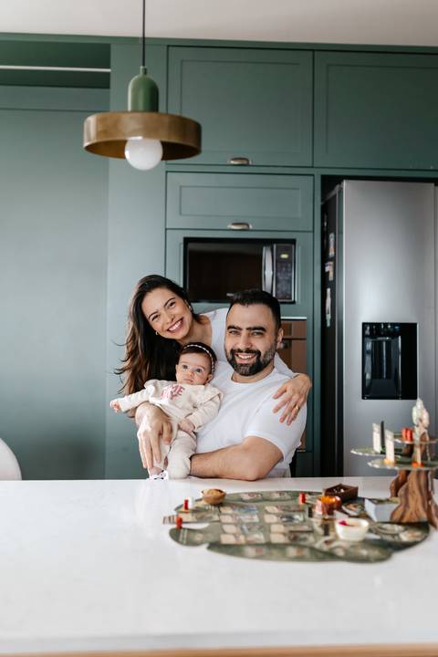 Retrato vertical da família sorrindo abraçada no centro da cozinha.'