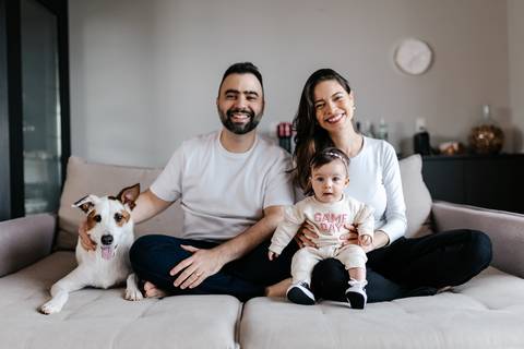 Retrato da família inteira sentada no sofá com o cachorro posando em primeiro plano.'