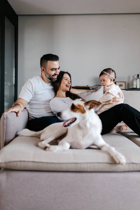 Pais sentados no sofá com a bebê enquanto o cachorro de estimação posa em primeiro plano.'