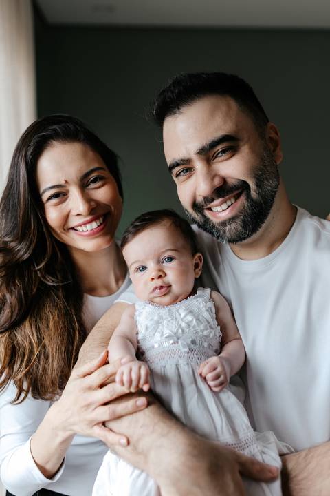 Close do casal sorridente com os rostos bem próximos ao da bebê.'