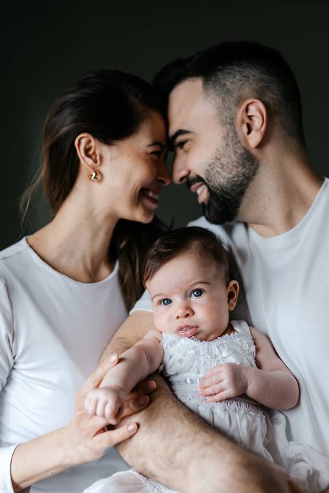 Pais encostando as testas com carinho enquanto olham para a bebê em seu colo.'