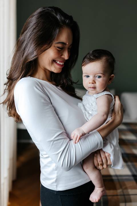 Close da mãe segurando a bebê com vestido rendado branco no colo.'