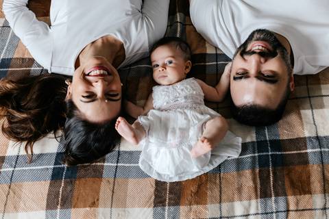 Foto aérea dos pais e da bebê deitados de costas na colcha xadrez da cama.'