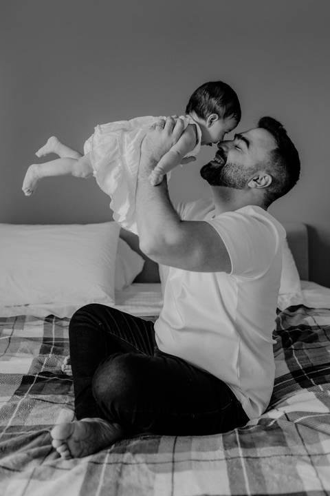 Versão artística em preto e branco do pai brincando de voar com a filha na cama.'
