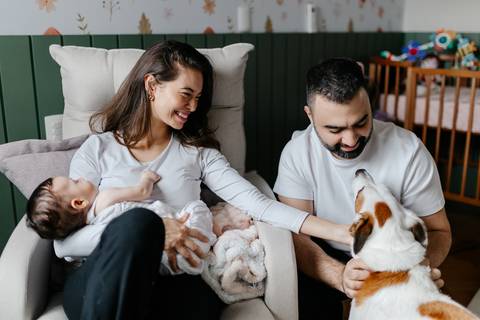 Pais sentados nas poltronas com a bebê enquanto fazem carinho no cachorro de estimação.'