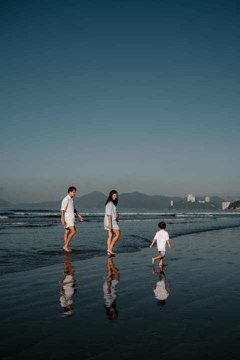 Foto de ângulo aberto da família caminhando na beira do mar com montanhas ao fundo.'