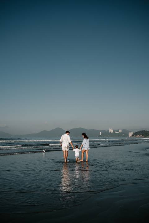 Foto de ângulo aberto da família caminhando de mãos dadas à beira do mar.'