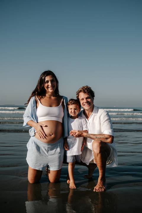 Retrato frontal da família reunida e sorridente com a água nos pés.'