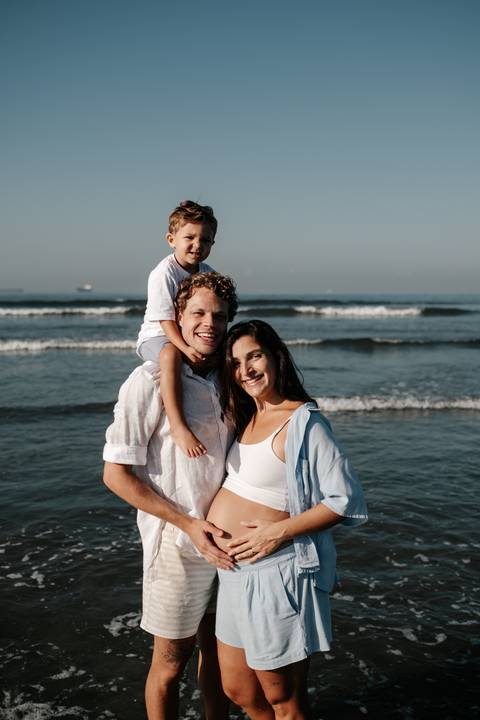 Retrato da família com o filho nos ombros do pai e a mãe sorrindo em destaque.'
