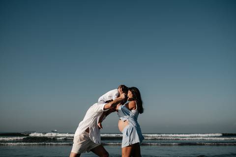 Casal se beijando carinhosamente com o mar e o céu azul ao fundo.'