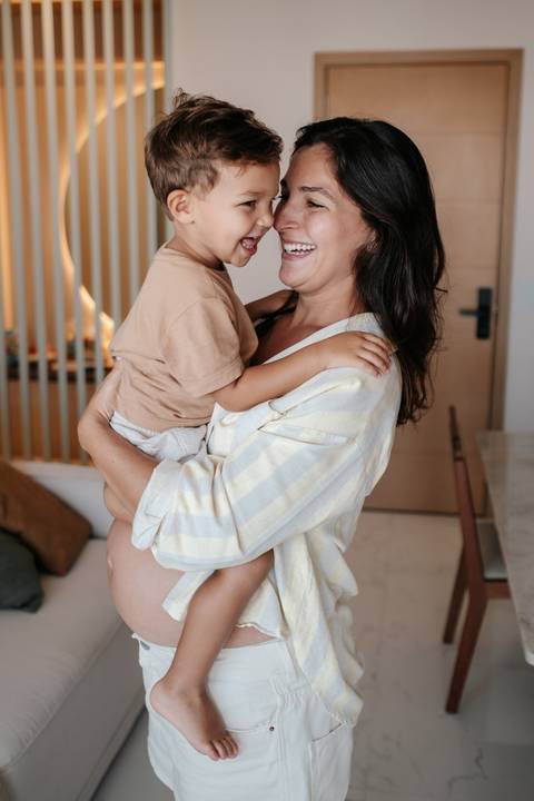 Mãe em pé segurando o filho pequeno no colo em um momento de carinho.'
