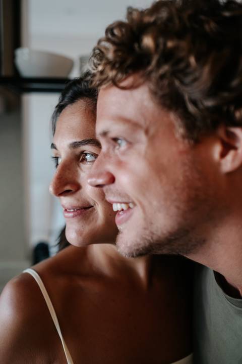 Close de perfil do rosto do casal sorrindo olhando na mesma direção.'