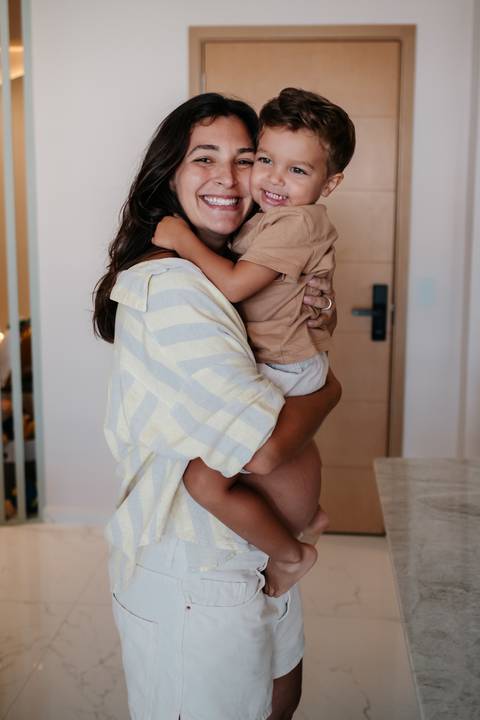 Close da mãe segurando o filho no colo de costas, destacando o abraço dele.'