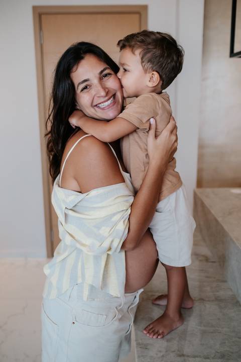Registro aproximado da mãe sorrindo com o filho aninhado em seu ombro.'