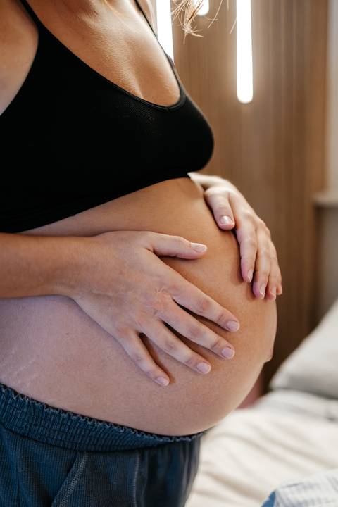Close-up das mãos amparando e tocando a barriga da gestante com carinho.'