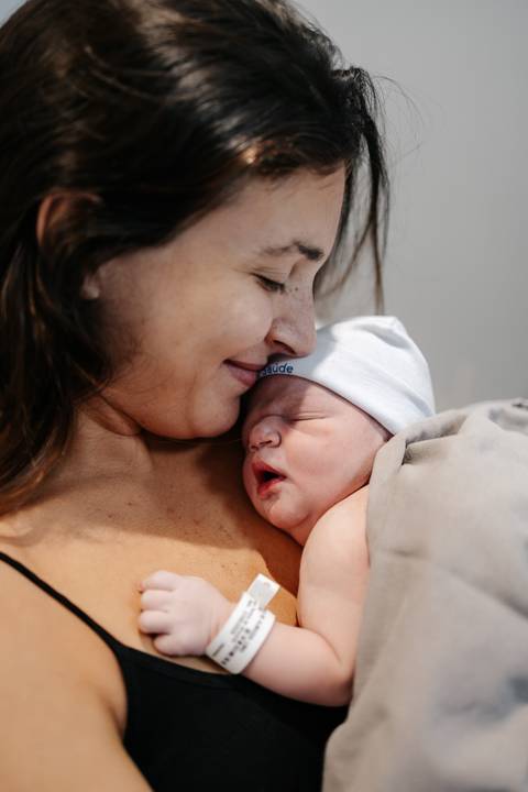 Mãe de perfil acolhendo o bebê recém-nascido com carinho contra o seu peito.'