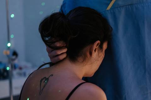 Costas da gestante sendo massageadas com foco em luzes terapêuticas no ambiente.'