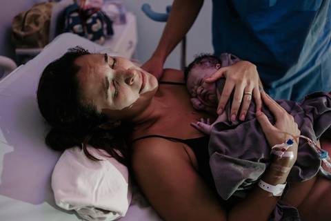 Registro emocionante da mãe com o bebê recém-nascido chorando sobre o seu peito logo após o nascimento.'