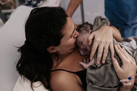 Close-up da mãe emocionada abraçando e beijando o seu bebê recém-nascido no peito.'
