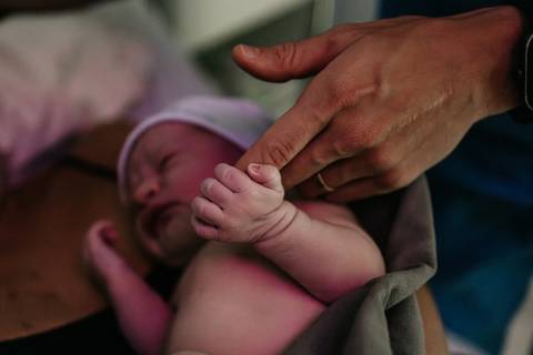 Detalhe da mão do pai tocando com suavidade a mãozinha do bebê recém-nascido.'