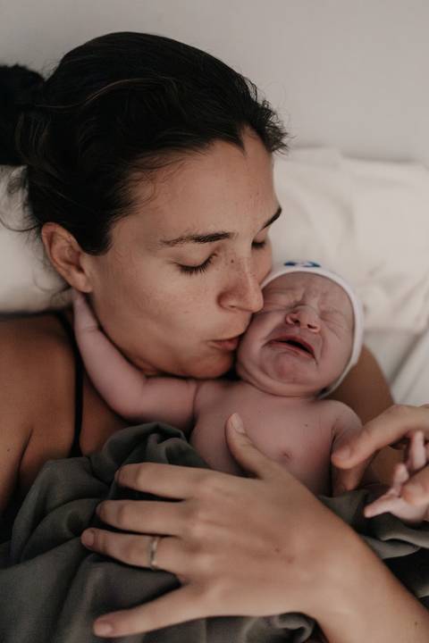 Mãe dando um beijo carinhoso na bochecha do bebê recém-nascido.'