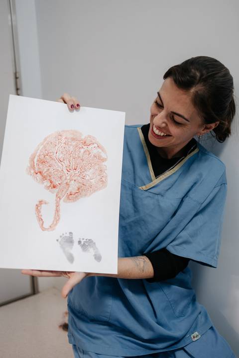 Profissional de saúde mostrando sorridente o carimbo da placenta feito em uma folha de papel.'