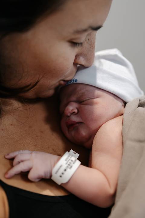 Close da mãe encostando o rosto e dando um beijo terno na cabeça do bebê com touquinha.'