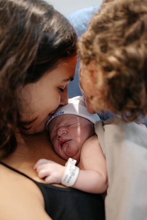 Pais aproximando os rostos juntos para dar um beijo carinhoso no bebê recém-nascido.'