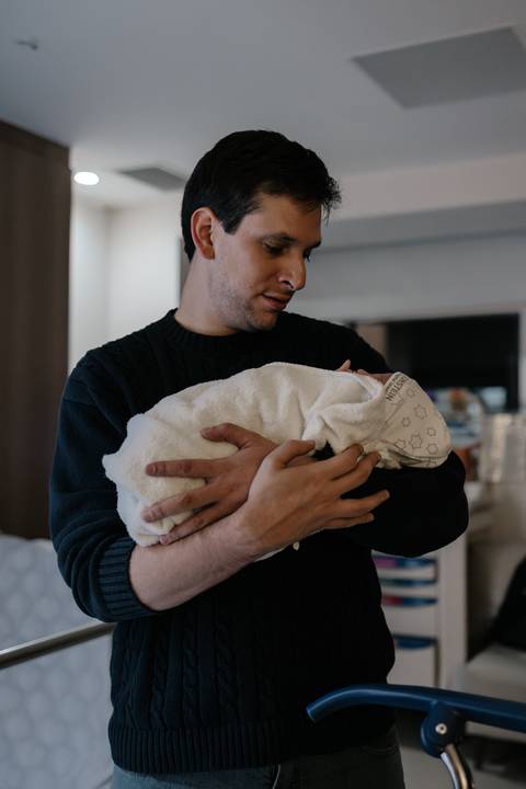 Pai segurando o bebê embalado na manta em seus braços no quarto.'