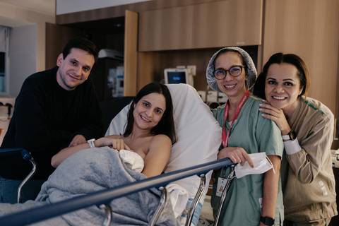 Foto em grupo da família com a médica e a equipe de enfermagem no hospital.'