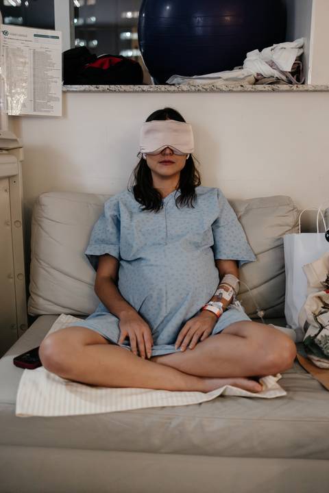 Gestante sentada de olhos vendados no sofá do hospital em momento de foco e meditação.'