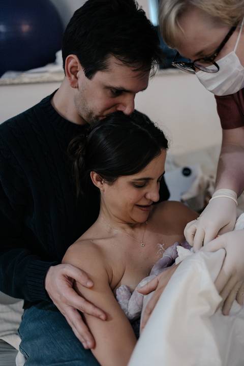 Mãe e pai olhando encantados para o recém-nascido no colo nos primeiros minutos de vida.'