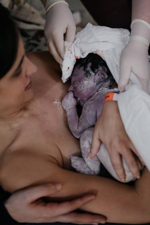 Ângulo superior do recém-nascido repousando sobre o peito da mãe no contato pele a pele.'
