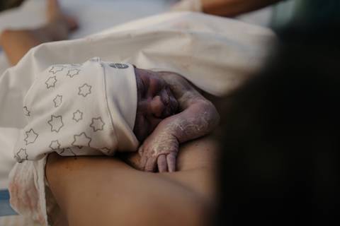 Recém-nascido com touquinha hospitalar descansando no colo da mãe.'