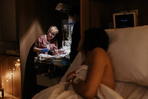 Mãe olhando a enfermeira fazendo os primeiros cuidados no bebê. '