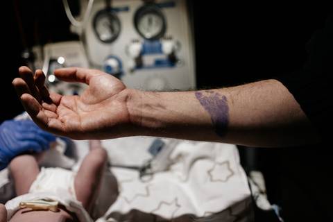 Carimbo da pezinhofobia com a pegada do bebê em tinta roxa no antebraço do pai.'