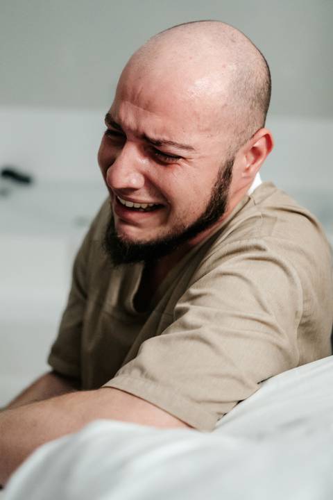 Parceiro chorando de emoção com o sorriso no rosto no momento exato do nascimento.'
