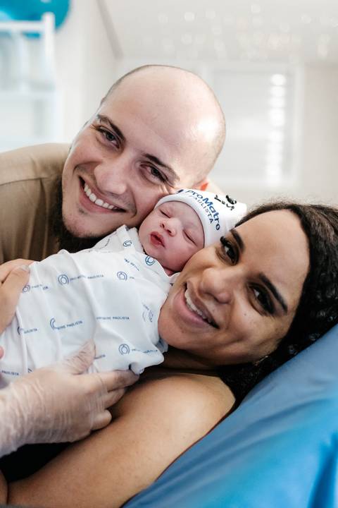 Retrato de perto do casal sorrindo feliz com o bebê encostado em seus rostos.'