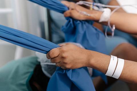 Mãos da gestante segurando com força o tecido de pano suspenso para tração durante a contração.'