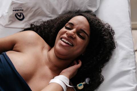 Gestante rindo aliviada e descontraída deitada na cama durante o trabalho de parto.'