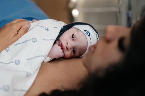 Visão de perfil da mãe e recém nascido com olho aberto. '