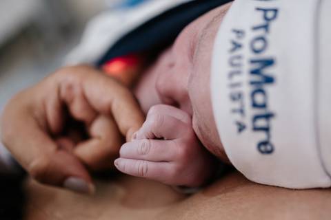 Detalhe em close-up das mãozinhas e dos dedos do bebê com a touca da maternidade Pro Matre.'