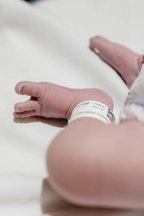 Detalhe do pezinho do bebê com a pulseira de identificação hospitalar.'