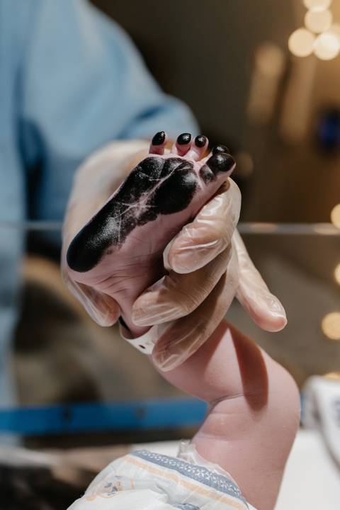 Profissional de saúde aplicando tinta preta na sola do pé do recém-nascido para a pezinhofobia.'