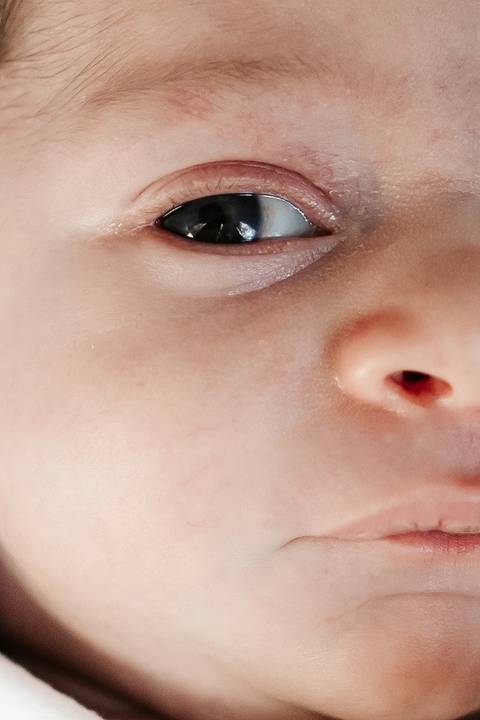 Macro em plano fechado focando no olho aberto e na pele do bebê.'