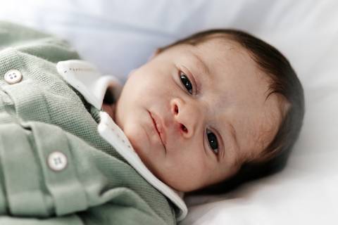 Bebê recém-nascido deitado de lado vestindo roupa verde e olhando fixamente para a câmera.'