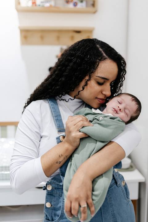 Mãe sorridente segurando o bebê adormecido aconchegado em seu peito.'